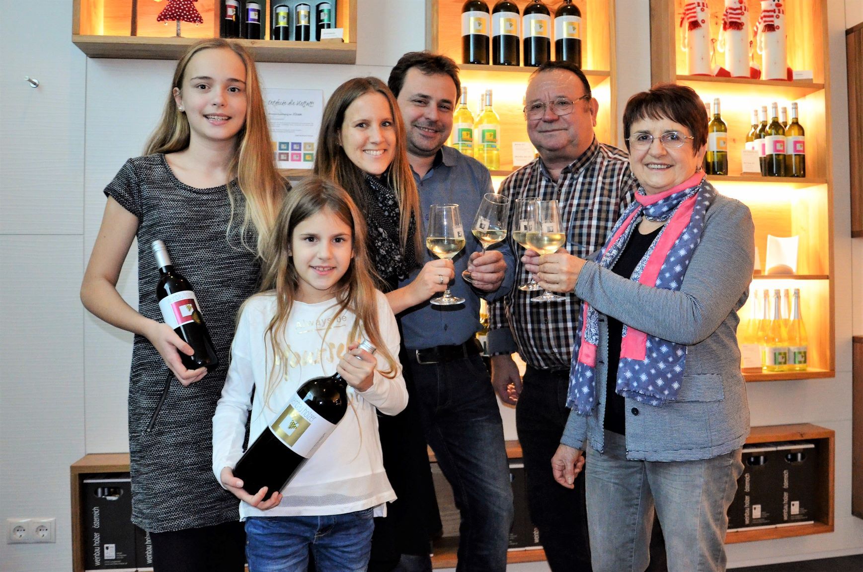 Familie mit Weinflaschen und Gläsern in einem Weinkeller.