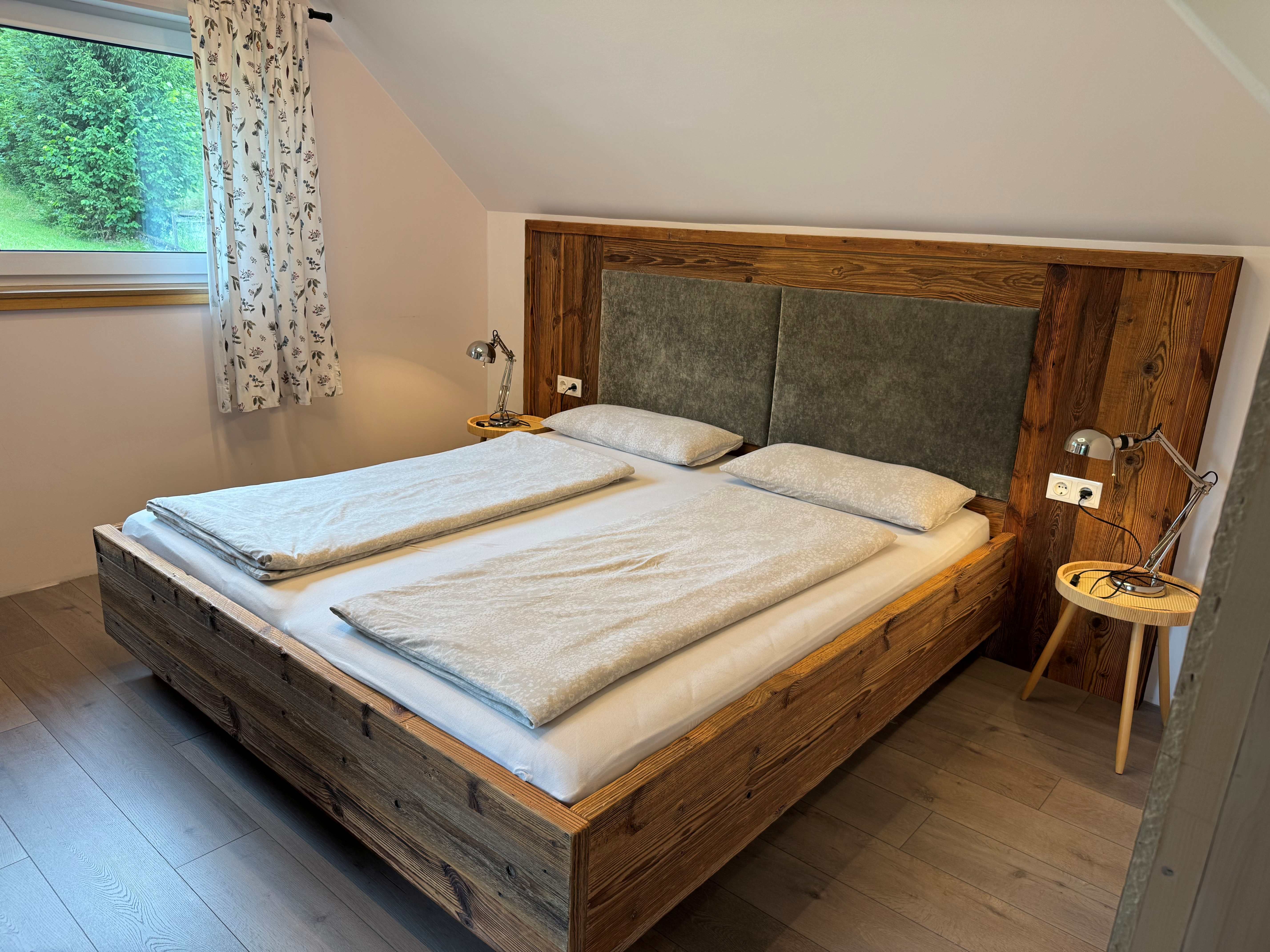 Ein gemütliches Schlafzimmer mit einem Doppelbett aus Holz, zwei Nachttischen mit Lampen und einem Fenster mit Vorhängen.