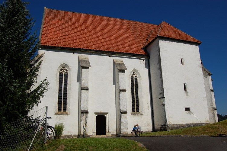 Weiße Kirche mit rotem Dach und gotischen Fenstern, blauer Himmel.