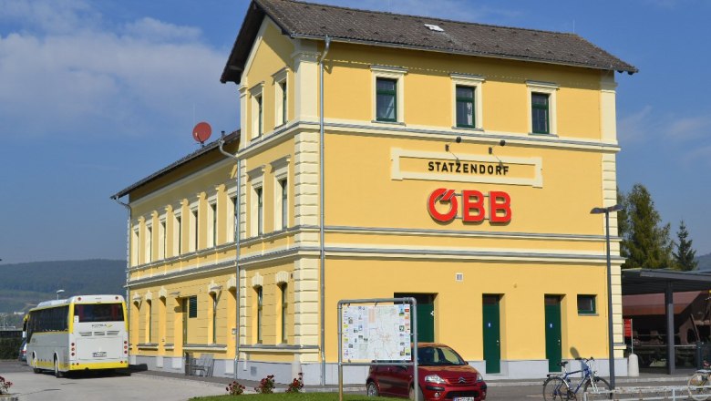 Gelbes Bahnhofsgeb&auml;ude mit &Ouml;BB-Logo und Bus im Vordergrund.