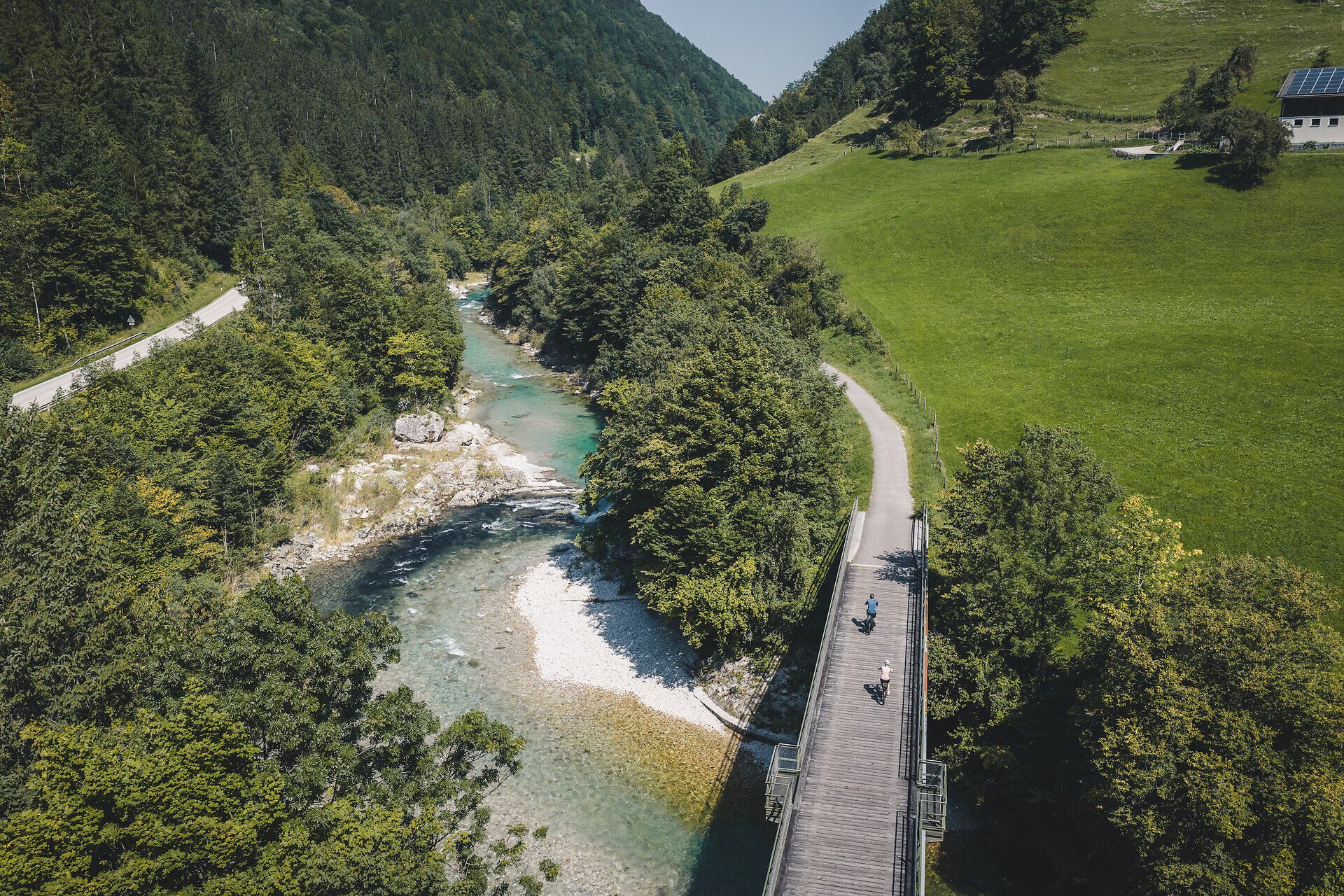 Zwei Radfahrende fahren auf einer Brücke entlang des Ybbstalradwegs, rundherum dichtes Gebüsch und unter der Brücke die klare Ybbs