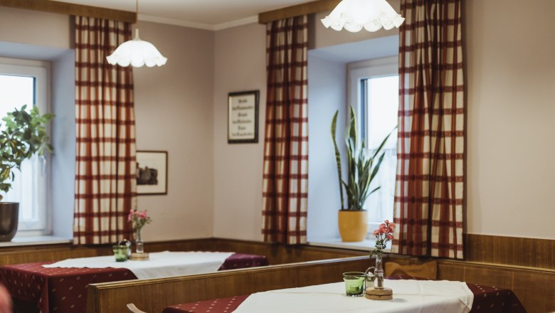 Gemütliche Wirtshausstube mit Holzmöbeln, karierten Vorhängen und dekorierten Tischen.