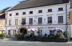 Historisches Gebäude mit Pizzeria und Restaurant, dekoriert mit Pflanzen und Sonnenschirmen.