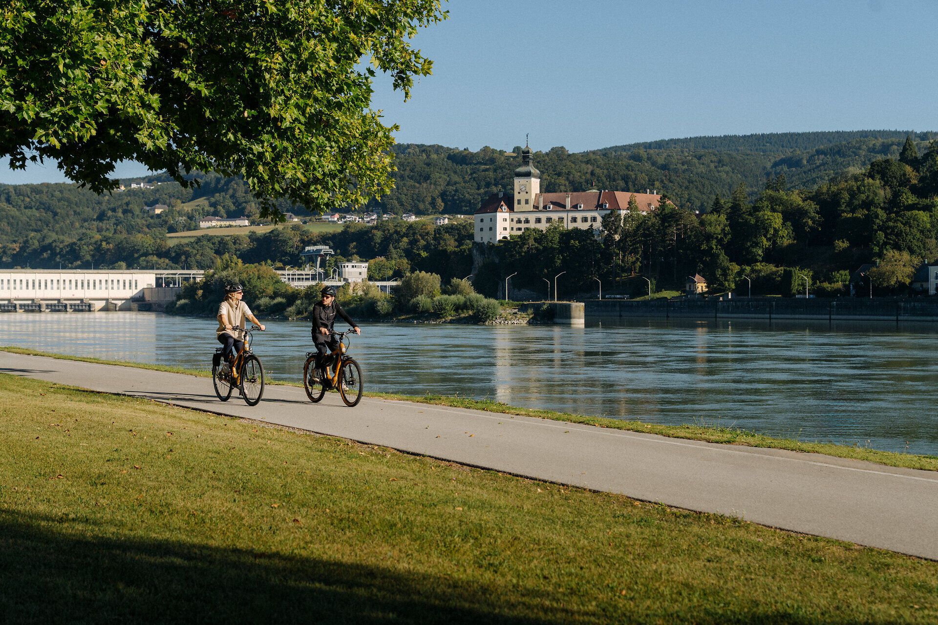 2 Radfahrer am Donauradweg in Ybbs mit Blick auf die Donau und Schloss Persenbeug unterwegs im Nibelungengau