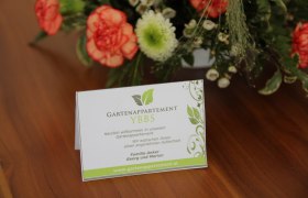 Willkommenskarte des Gartenappartements Ybbs auf einem Tisch mit Blumen.