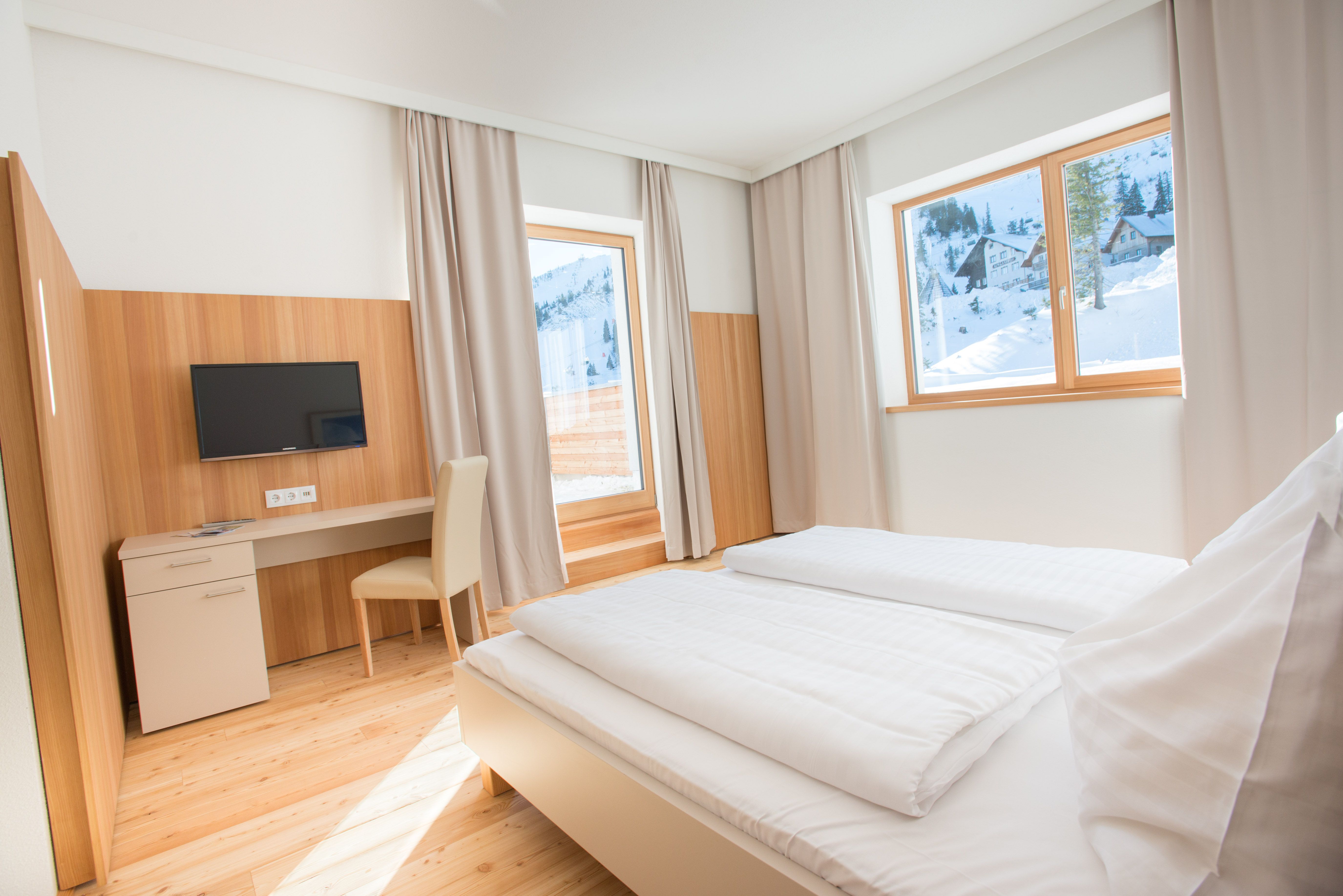 Helles Hotelzimmer mit Doppelbett, Schreibtisch und Blick auf verschneite Berge.