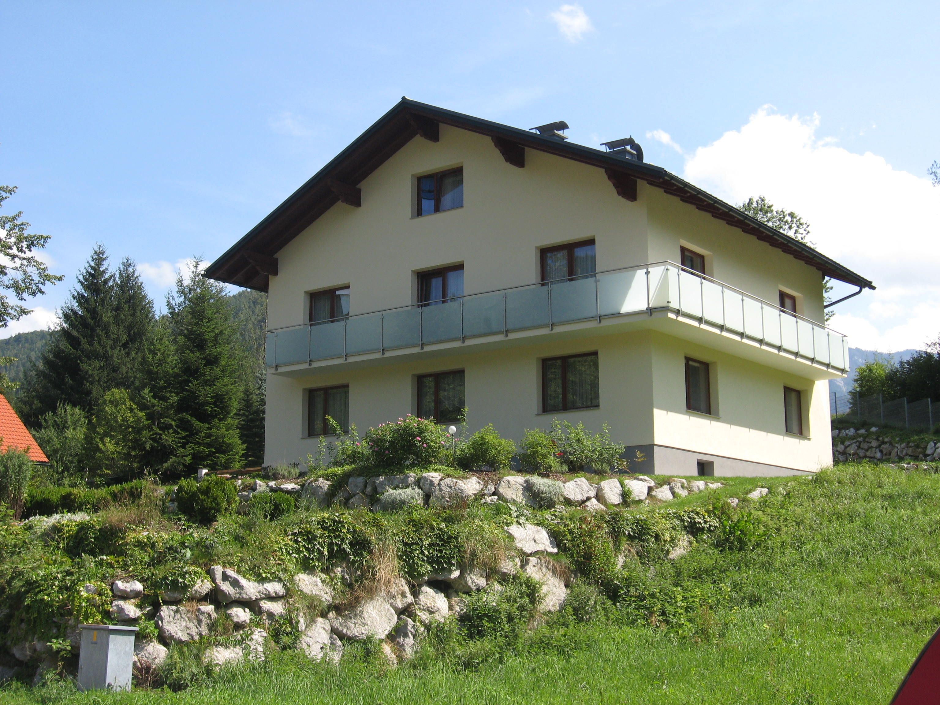 Ein zweistöckiges Haus mit Balkon in einer grünen, hügeligen Landschaft.