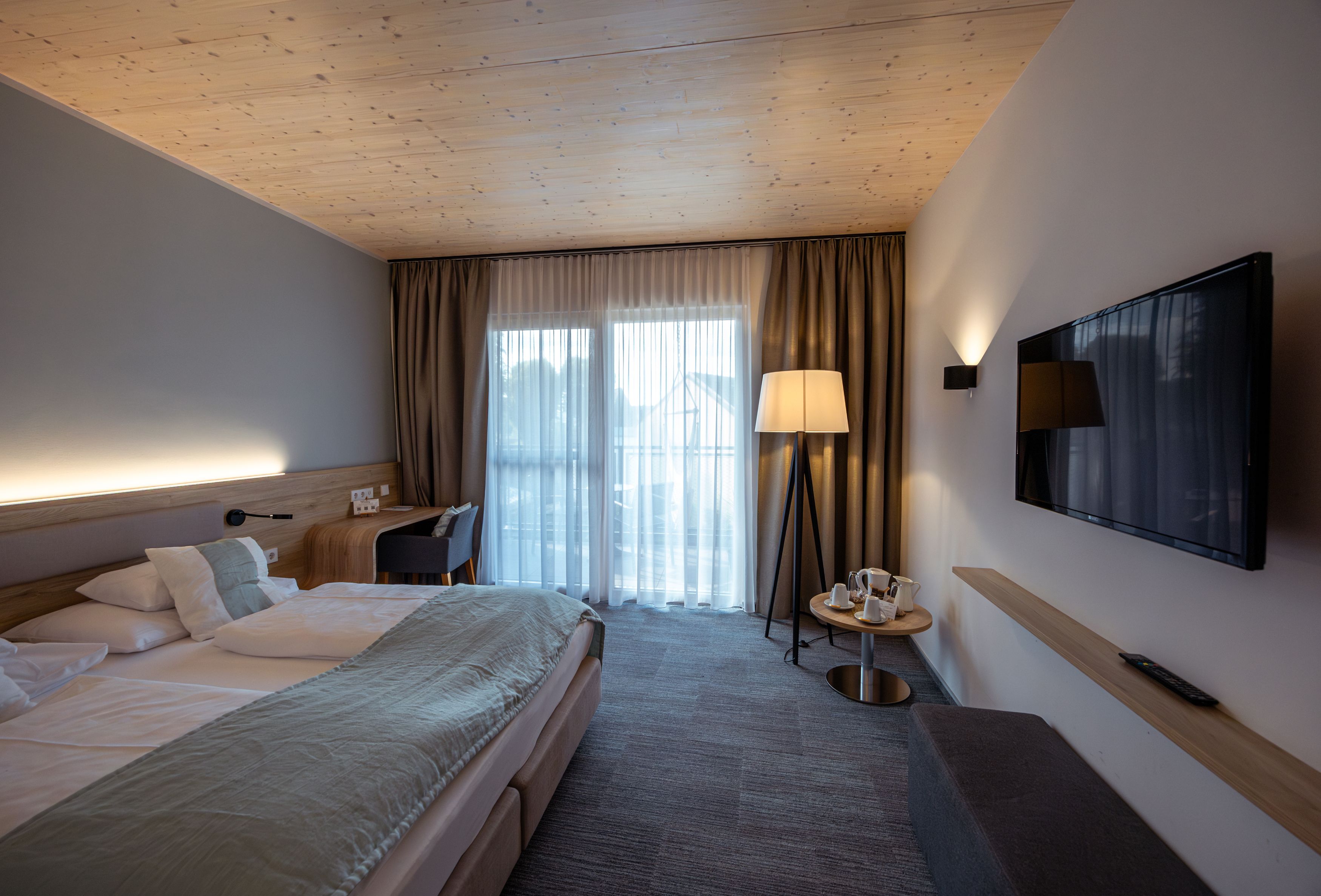 Modernes Hotelzimmer mit Doppelbett, Fernseher, Stehlampe und Balkon.