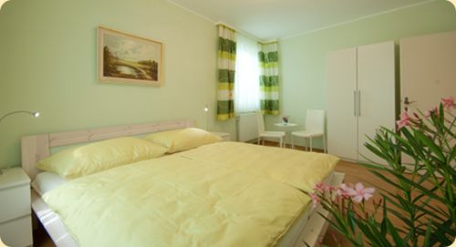 Ein hellgrünes Schlafzimmer mit Doppelbett, weißen Möbeln und einem Bild an der Wand.