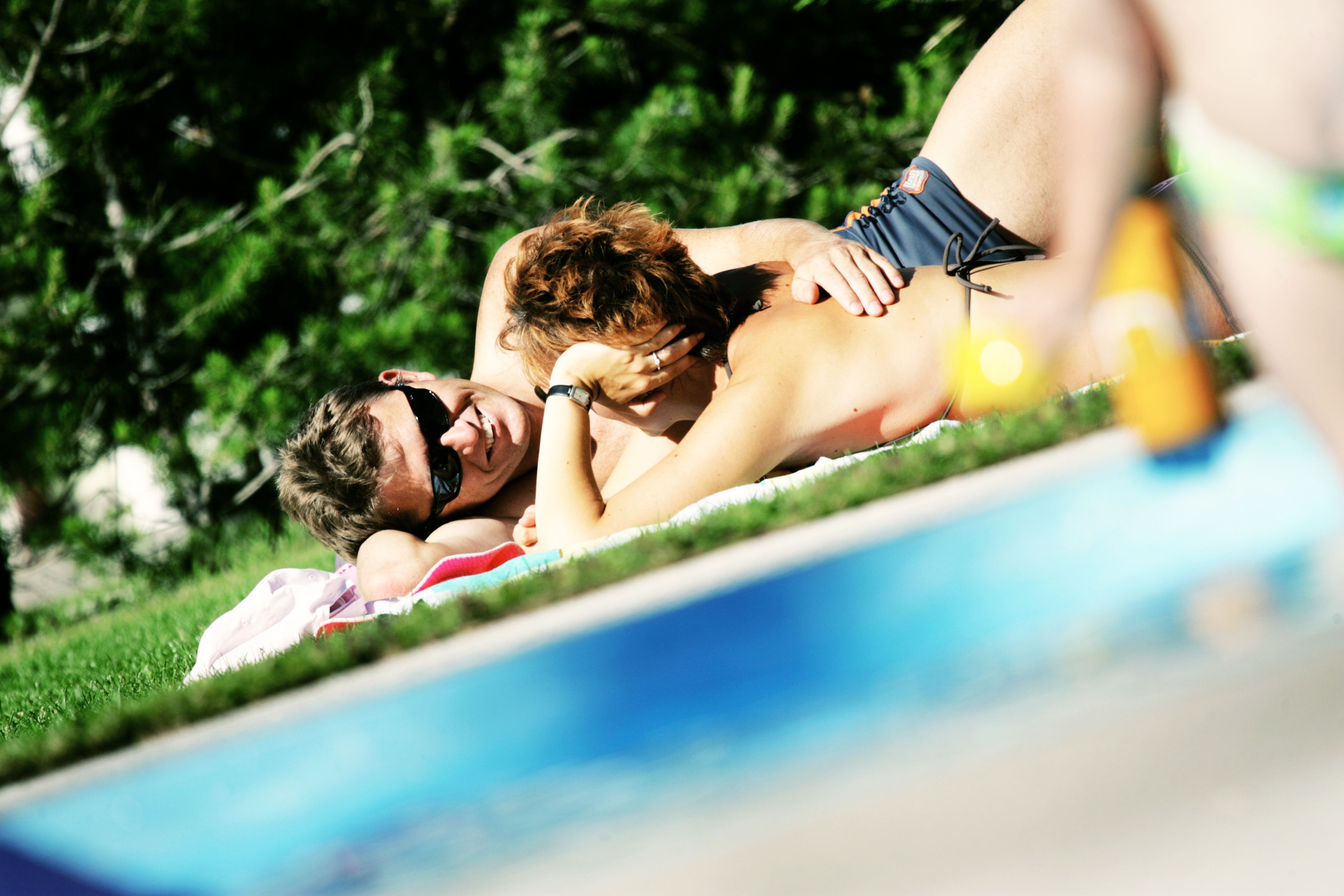 Ein Paar liegt entspannt auf einer Wiese neben einem Pool.