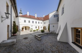 Innenhof der TDR-FineArtGallerie in Traismauer mit Kopfsteinpflaster und weißen Gebäuden.