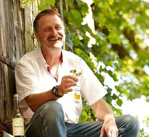 Mann sitzt draußen mit einem Glas Wein in der Hand, umgeben von grünen Pflanzen.