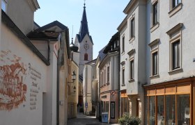 Schmale Gasse mit alten Gebäuden und Kirchturm im Hintergrund.