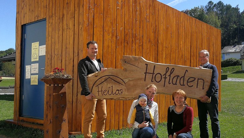 Familie vor einem Holzgebäude mit einem Schild 'Heilos Hofladen'.