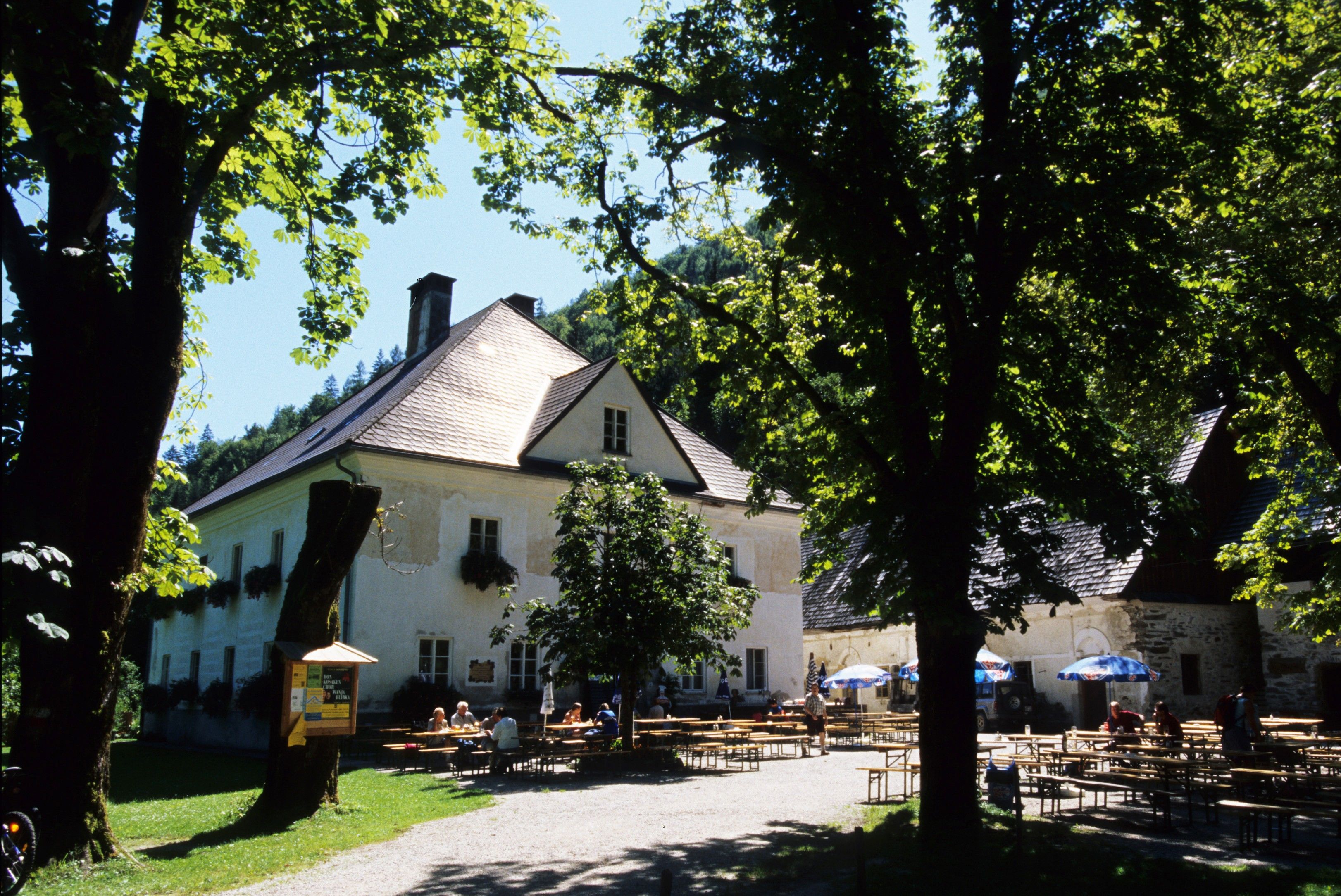Ein Herrenhaus mit Biergarten im Grünen, umgeben von Bäumen.