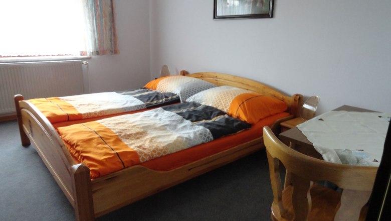 Zimmeransicht, © Schreiblehner Ein einfach eingerichtetes Schlafzimmer mit zwei Einzelbetten, einem Tisch und einem Stuhl.