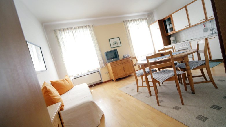 Helles Wohnzimmer mit Sofa, Esstisch und Küchenzeile.