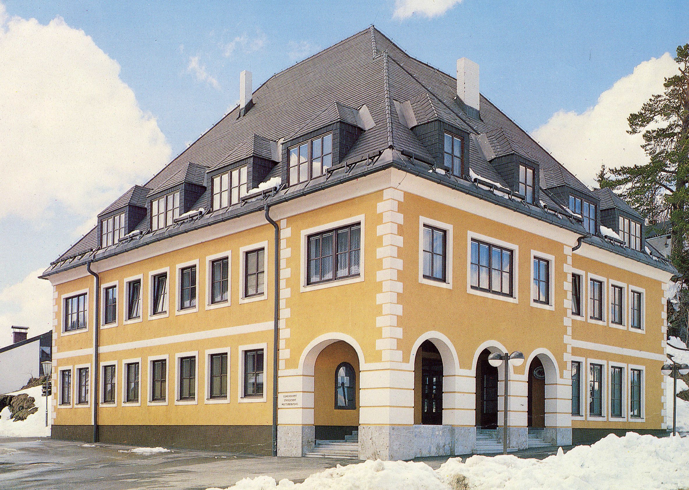 Gelbes Gebäude mit grauem Dach und vielen Fenstern, umgeben von Schnee.