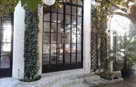 Eingangsbereich mit großen Glasfenstern, Efeu und Pflastersteinen.