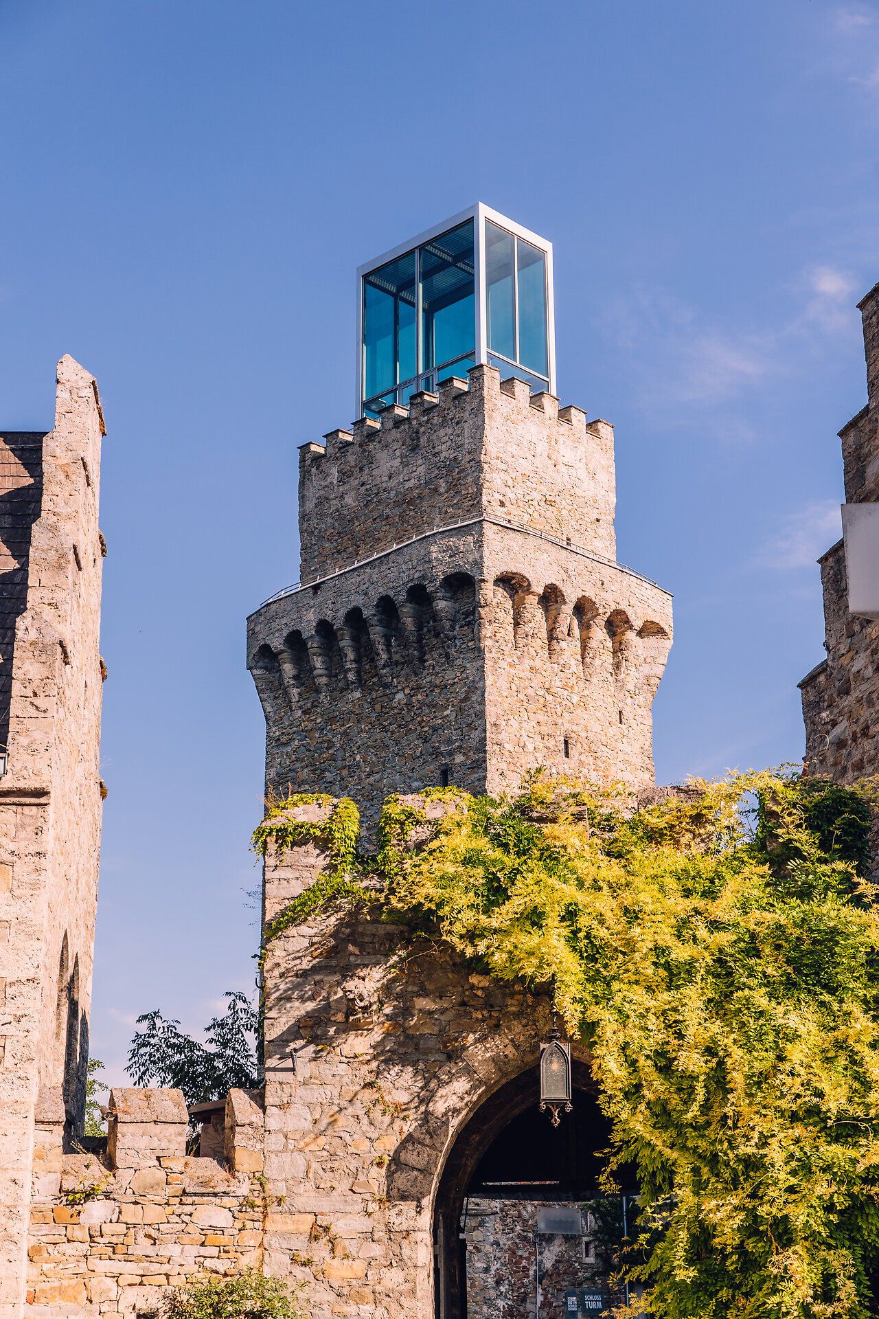 Historischer Stadtturm in Waidhofen an der Ybbs mit moderner Glaskonstruktion auf der Turmspitze, umgeben von alten Steinmauern und grüner Bepflanzung.