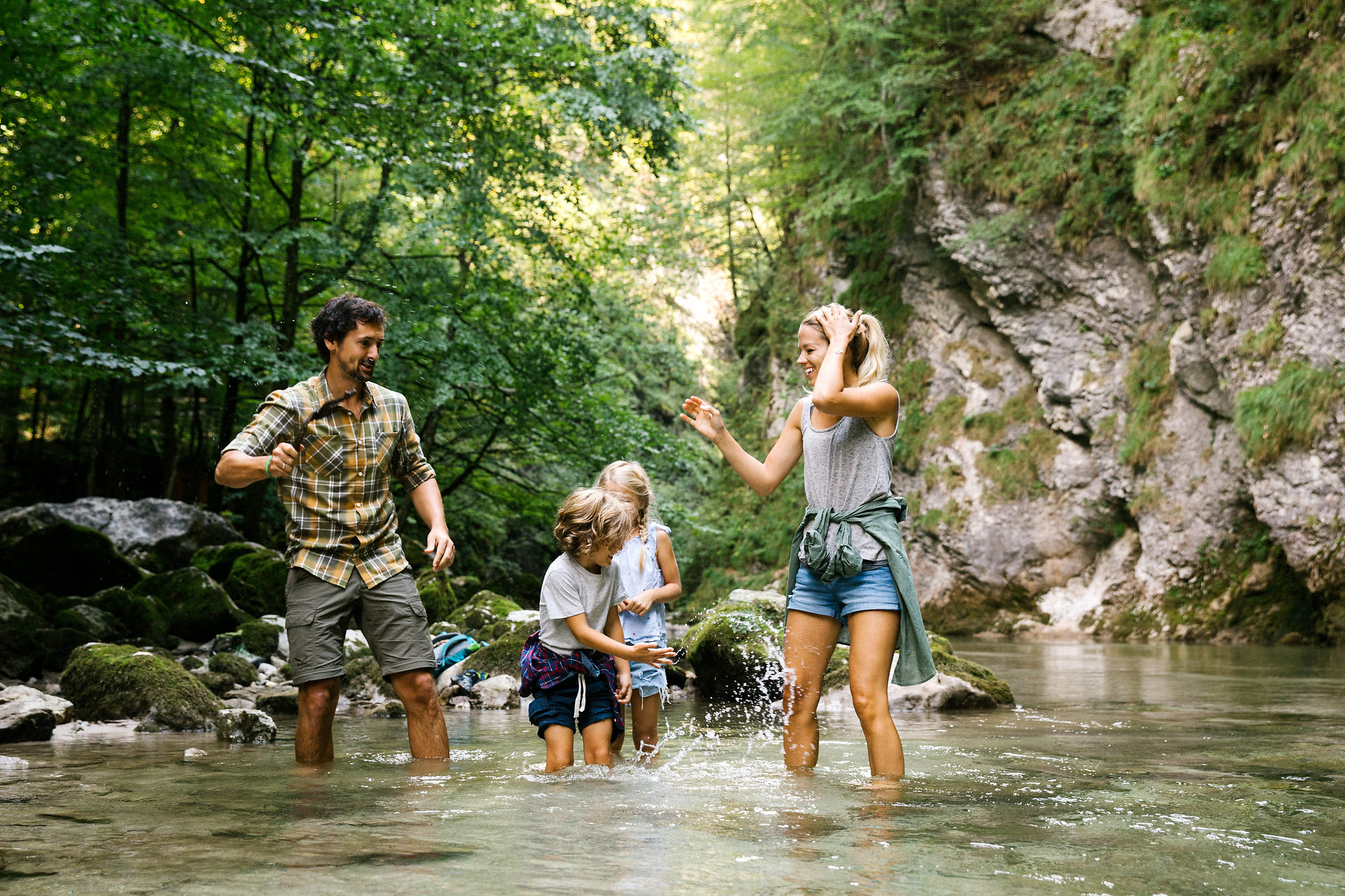 Eine fröhliche Familie genießt einen unbeschwerten Tag im klaren Wasser eines plätschernden Baches. Umgeben von üppigem Grün und majestätischen Felsen, spritzen die Kinder lachend Wasser, während die Erwachsenen die erfrischende Natur erleben. Hier im Naturpark Ötscher Tormäuer wird der Sommer in seiner schönsten Form zelebriert.