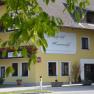 Yellow building with sign 'Landgasthof Kammerhof', flower boxes and trees in the foreground.
