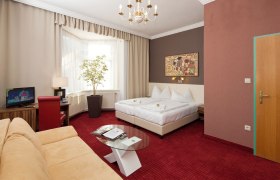 Hotelzimmer mit Doppelbett, rotem Teppich, Sofa, Fernseher und großem Fenster.