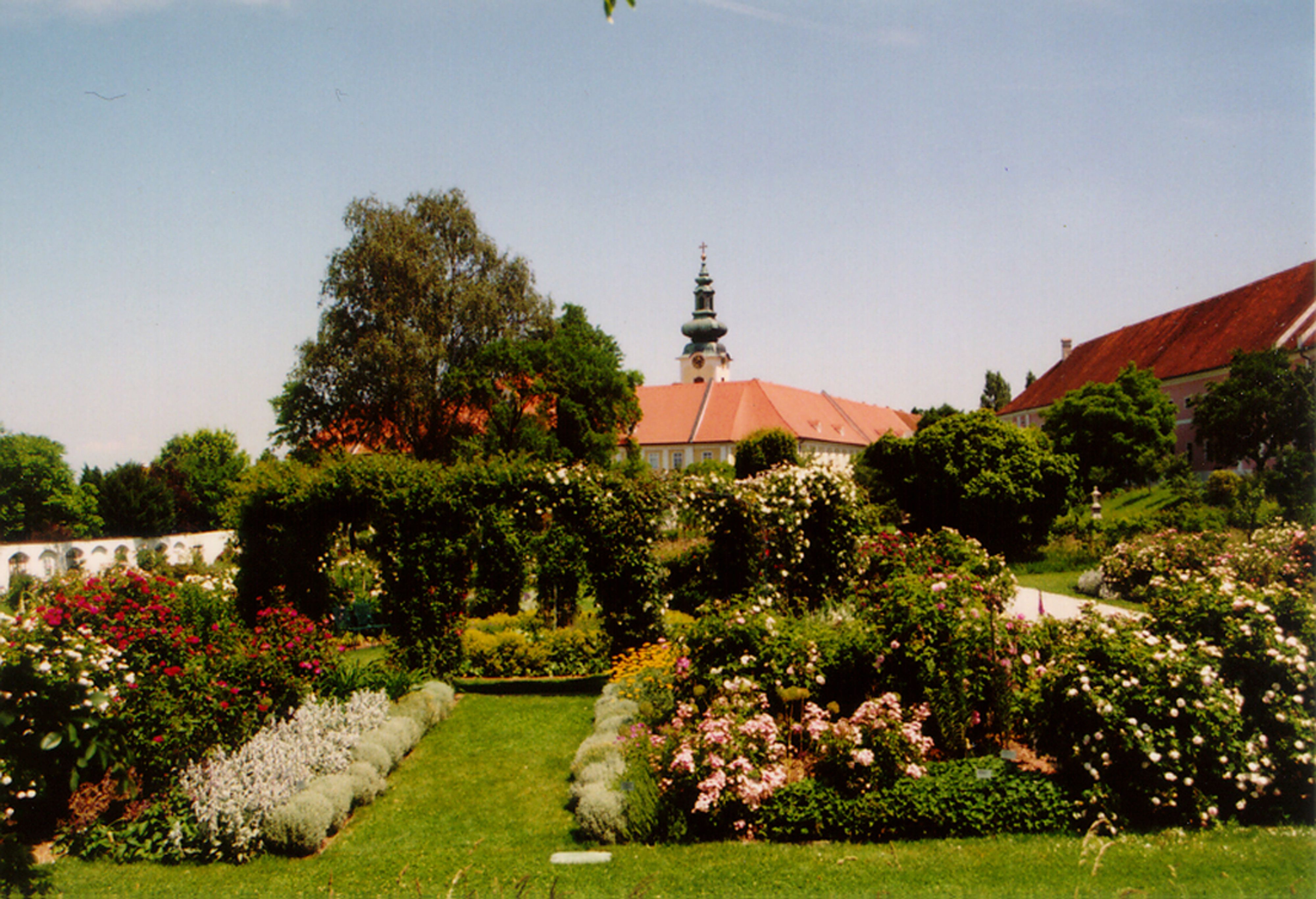 Historischer Garten mit Blumen und Bäumen, im Hintergrund ein Gebäude mit Turm.