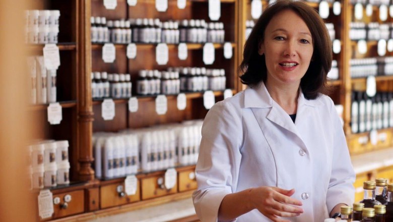 Woman in a white coat in a traditional pharmacy with shelves full of bottles.