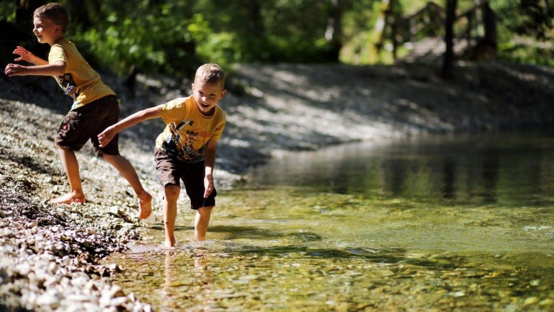 Two children play in nature on the banks of clear water.