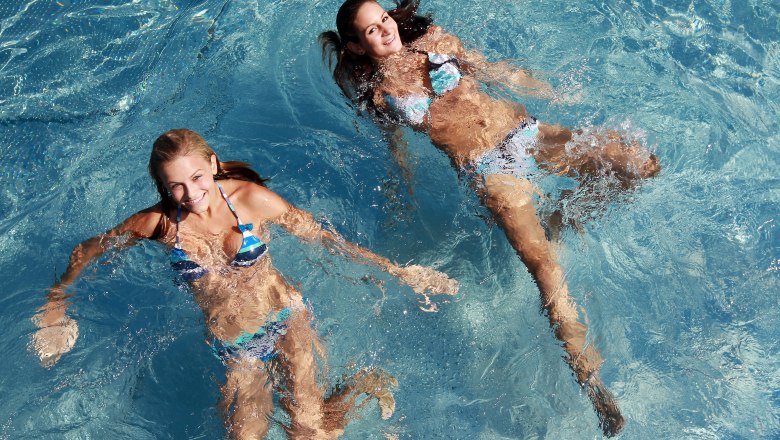 Two women swim in a pool and smile at the camera.