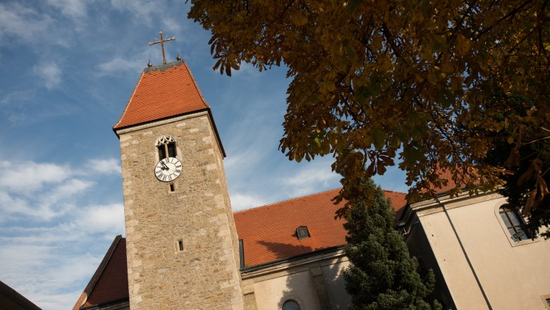 Kirchturm der Kirche Weißenkirchen mit Uhr und rotem Dach, umgeben von Herbstlaub und blauem Himmel.