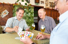 Three men playing cards in an inn with a green tiled stove in the background.