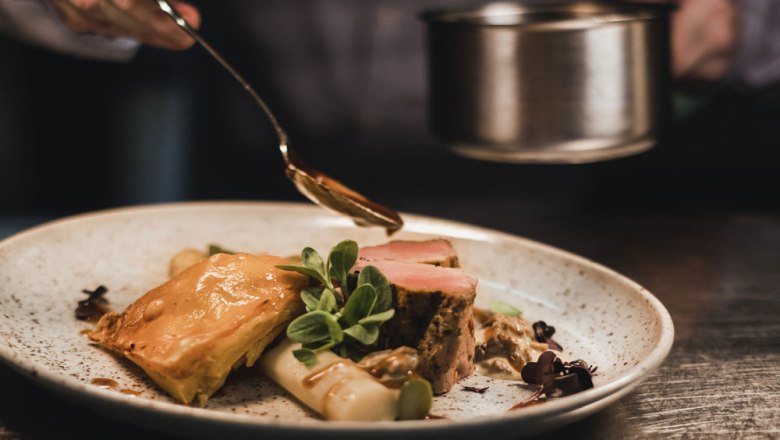 Ein Teller mit Kalbsmedaillons, Spargel und Blätterteig, garniert mit Sauce und Kräutern.