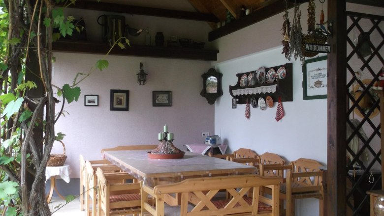 Covered terrace with table and chairs, in the background a wall with various wall decorations.