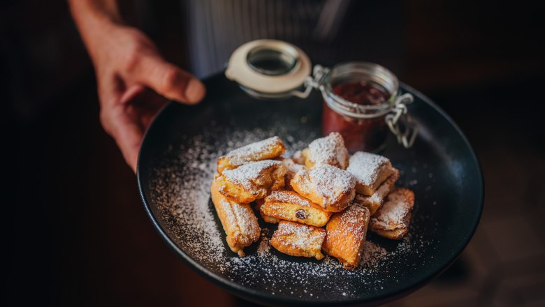Ein Teller mit Kaiserschmarren, bestäubt mit Puderzucker, und einem Glas Zwetschkenröster.