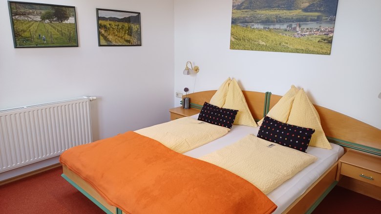 Gemütliches Hotelzimmer mit Doppelbett, orangefarbener Decke und Landschaftsbildern an der Wand.
