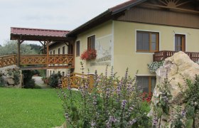 Ein gelbes Geb&auml;ude mit Holzbalkon und Blumen, umgeben von gr&uuml;ner Landschaft.