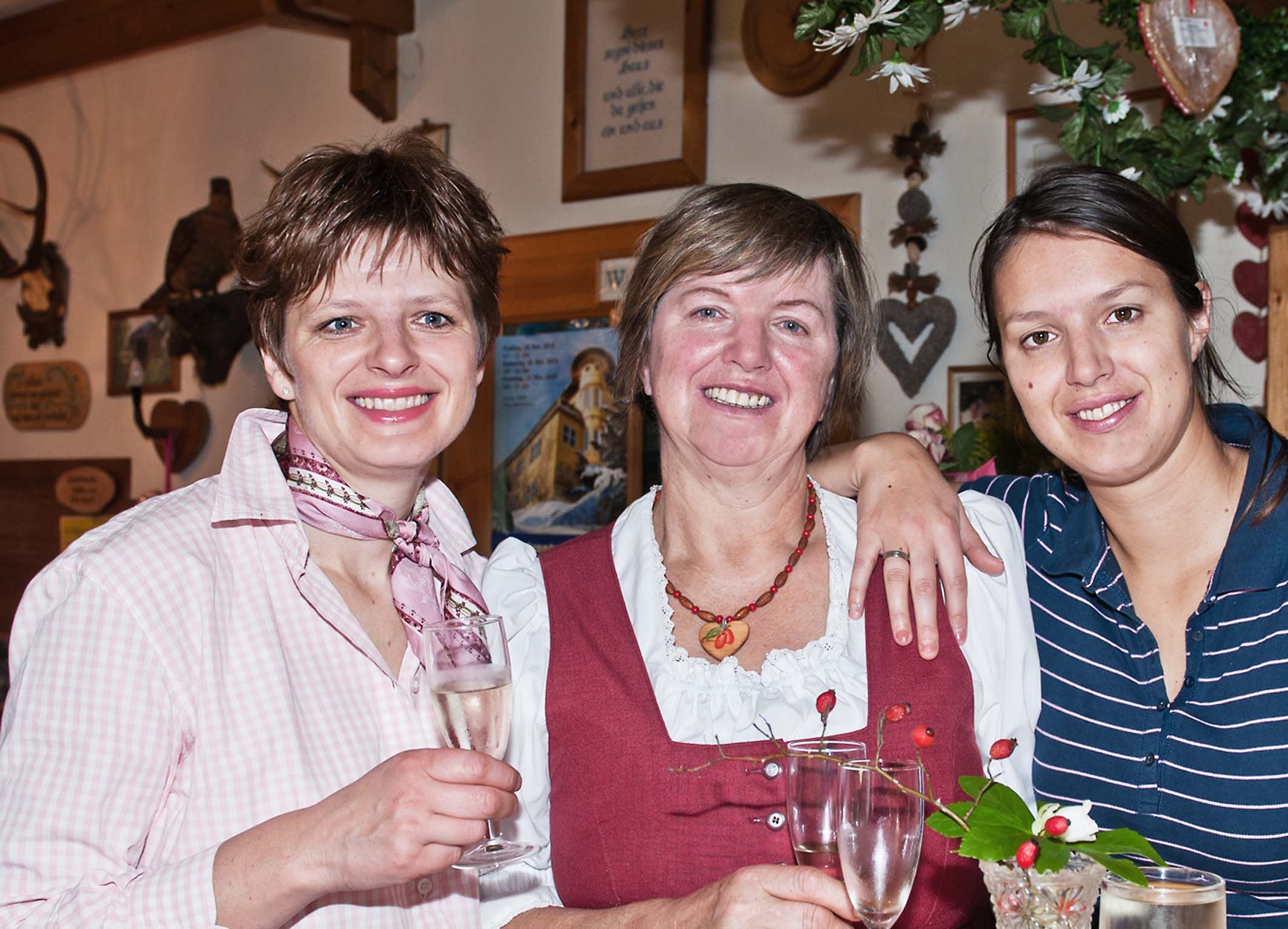 Drei Frauen lächeln in die Kamera und halten Sektgläser in der Hand.