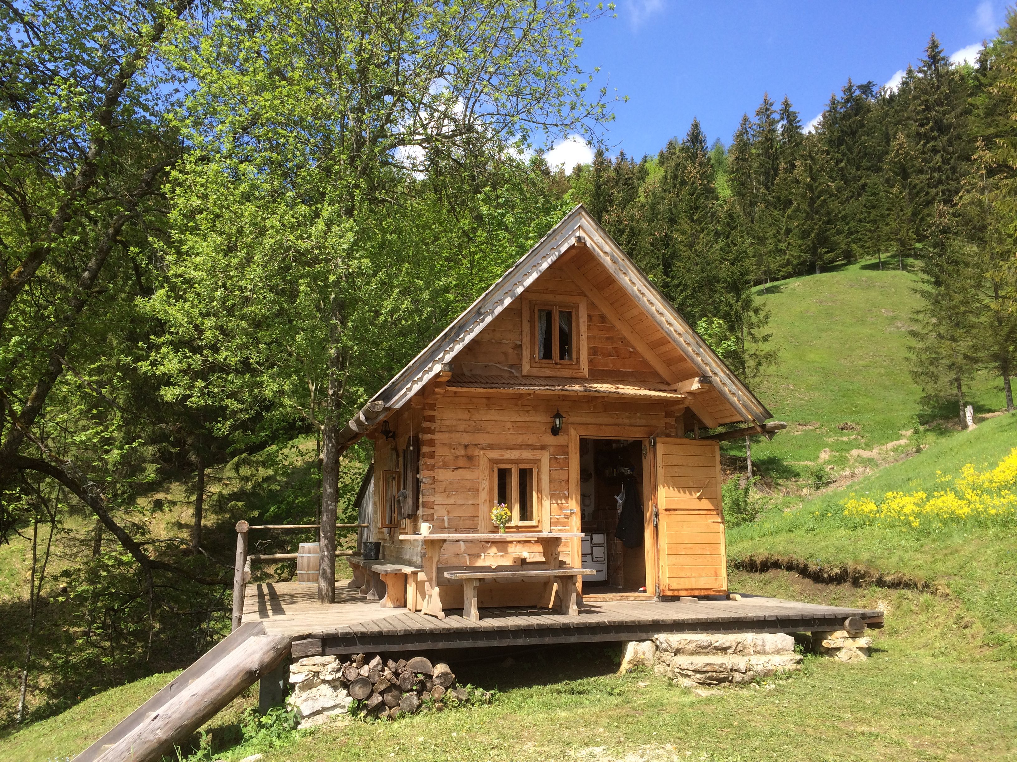 Eine kleine Holzhütte in einer grünen, bewaldeten Landschaft mit blauem Himmel.