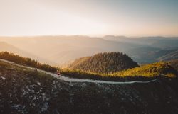 Ein Trailläufer läuft auf einem schmalen Steinweg in der Abendsonne mit Blick in die umliegenden Bergwelt.