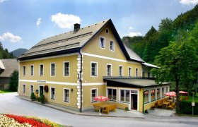 Ein gelbes Gasthaus mit Terrasse und Sonnenschirmen, umgeben von Bäumen.