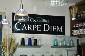 Innenansicht einer Bar mit einem Schild 'Cocktailbar Carpe Diem' an der Wand.