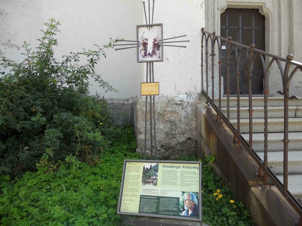 Ein Schild mit Informationen zum Annaberger Kreuzweg neben einer Treppe und Pflanzen.