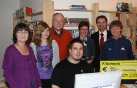 Gruppe von Menschen in einer Bücherei mit einem Scheck über 150 Euro.