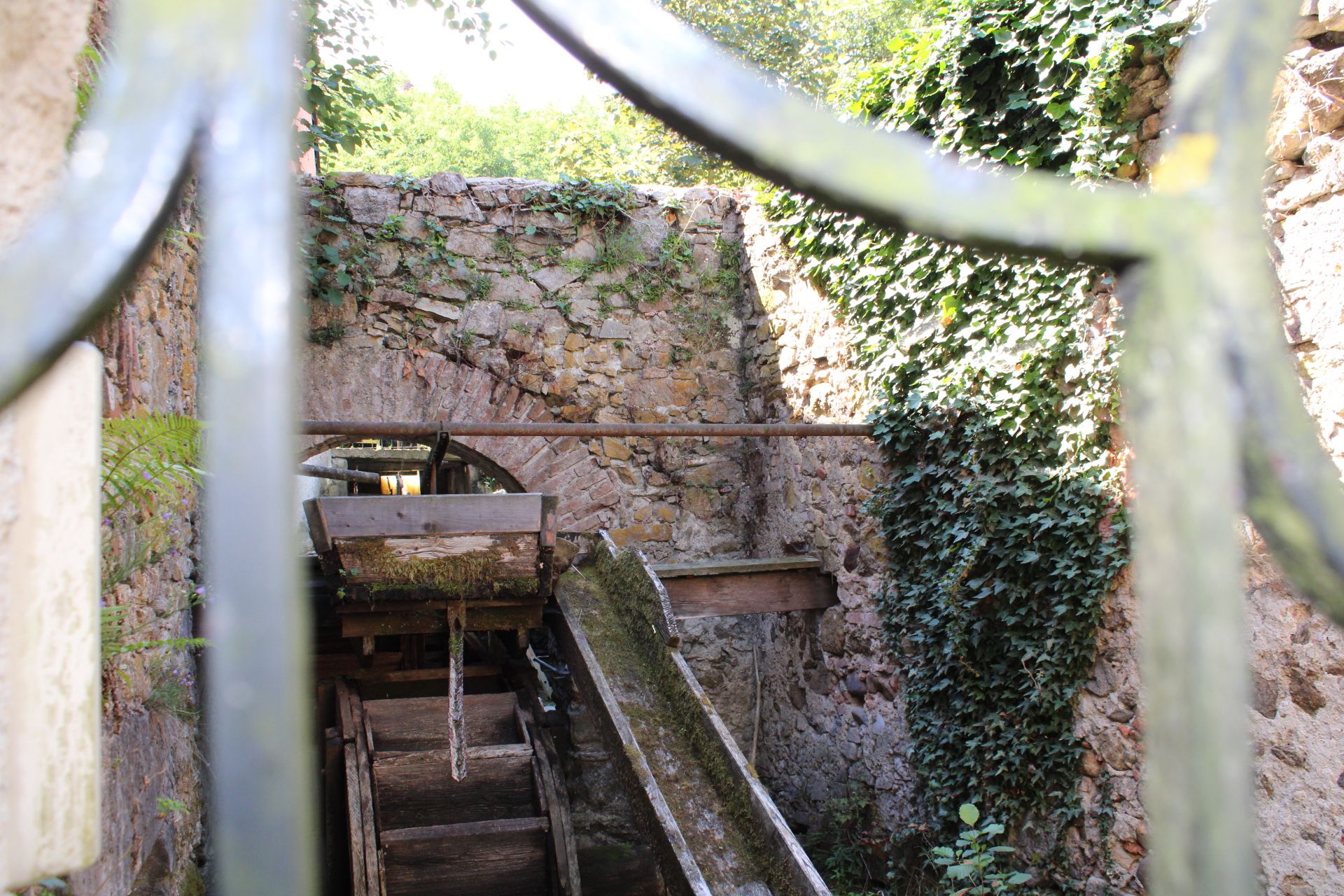 Detail einer alten Hammerschmiede mit Wasserrad und Efeu-bewachsenen Steinmauern.