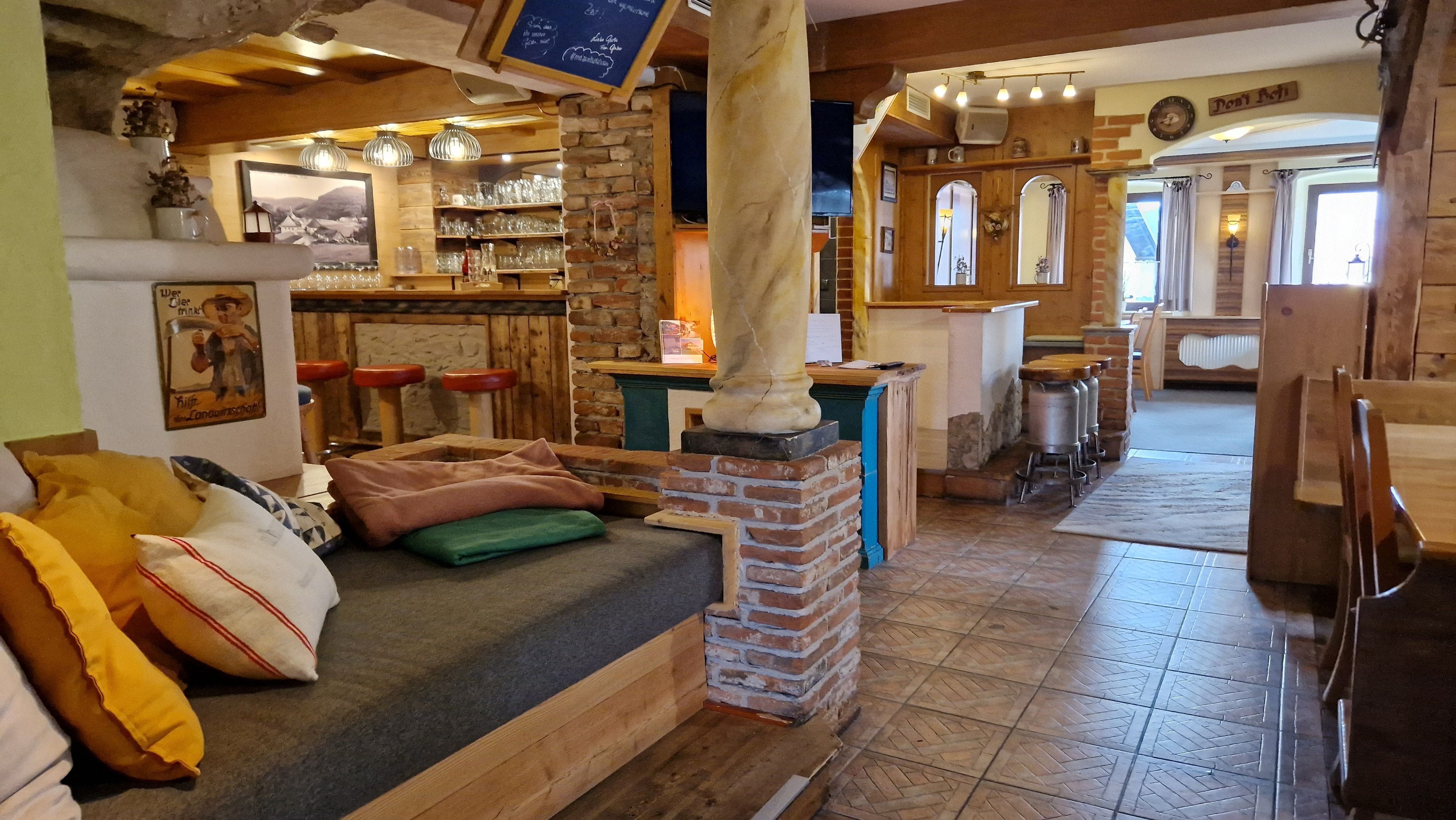 Aufenthaltsbereich mit rustikaler Einrichtung, Holzmöbeln und einer Bar mit roten Hockern.