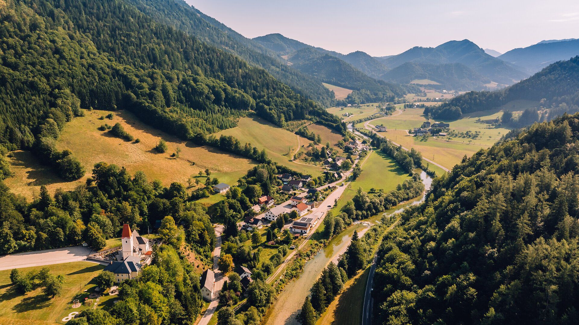 Luftbildaufnahme von St. Georgen am Reith, umgeben von Wäldern, grünen Wiesen und Bergen.