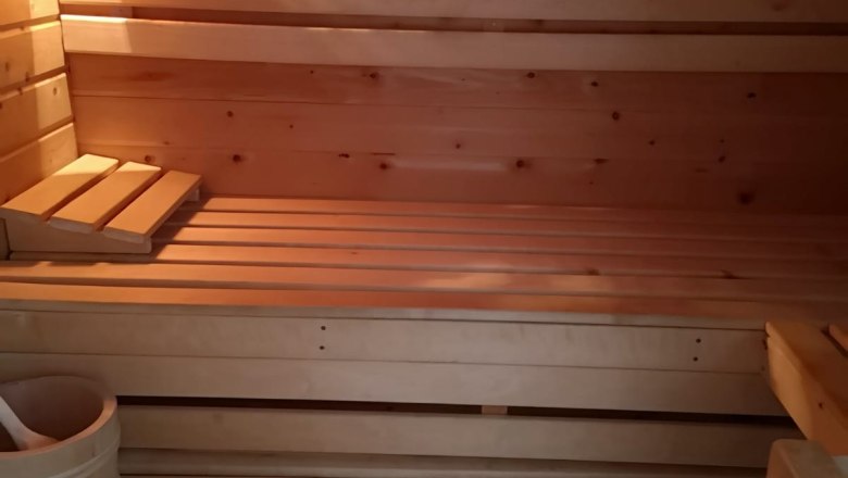 Innenansicht einer Holzsauna mit Bänken, Thermometer und Eimer.