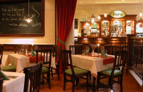 Gem&uuml;tliches Restaurant mit Holzm&ouml;beln, gedeckten Tischen und einer Bar im Hintergrund.